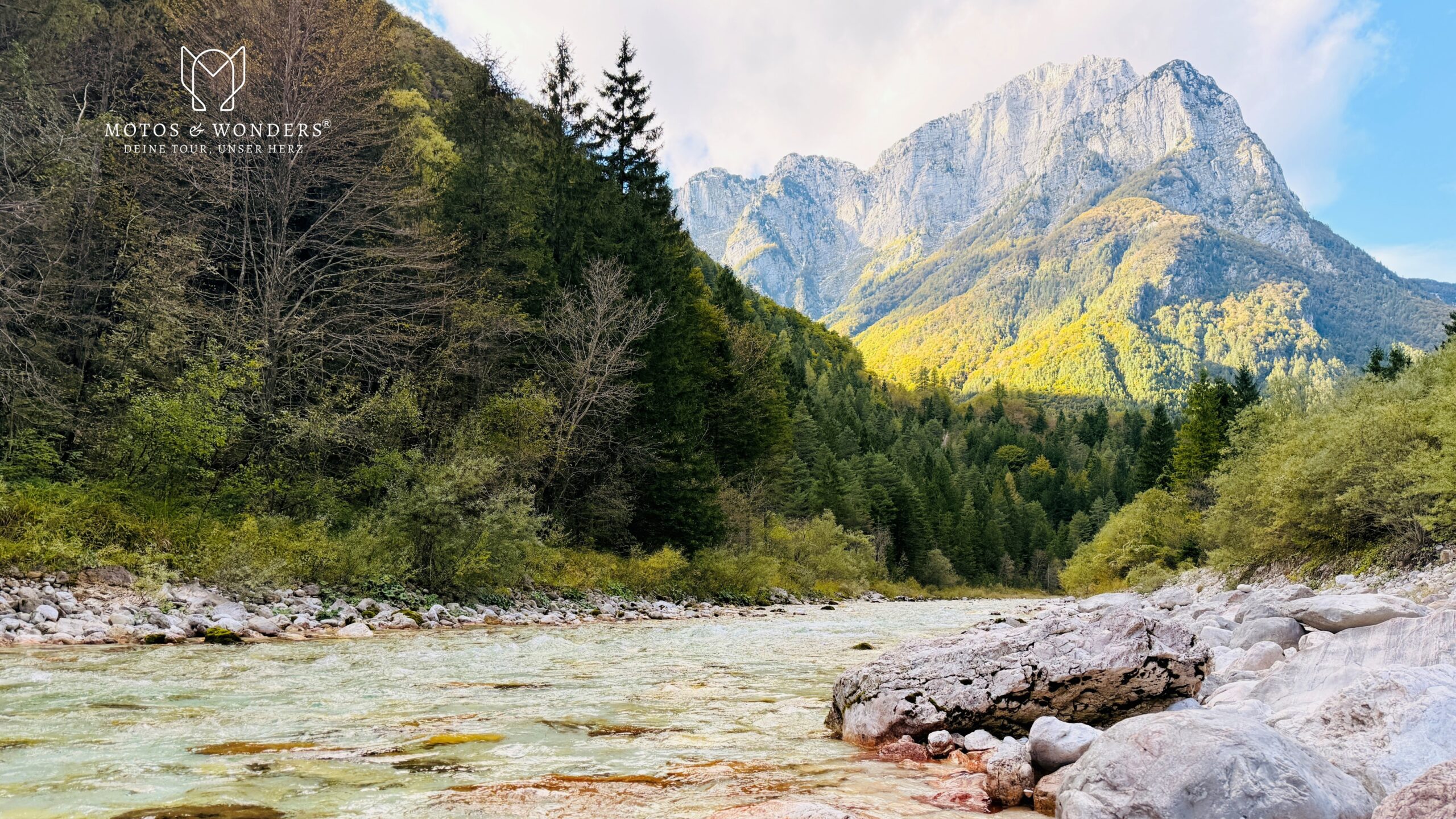 Turquoise mountain stream before forested slopes and a striking alpine rock face.
