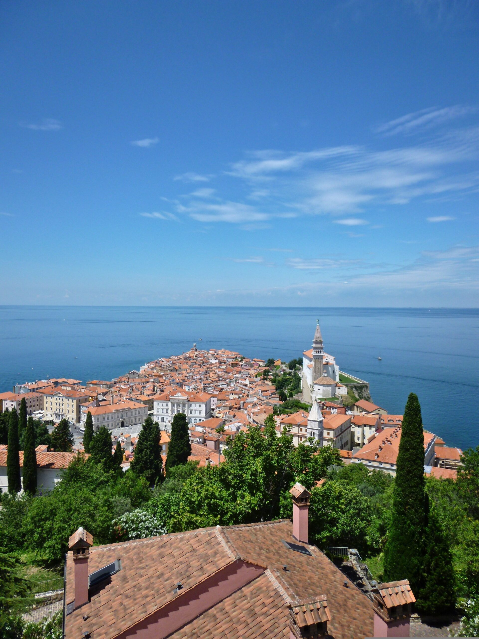 Panoramic view of Piran old town with terracotta rooftops, church bell tower and the Adriatic Sea.