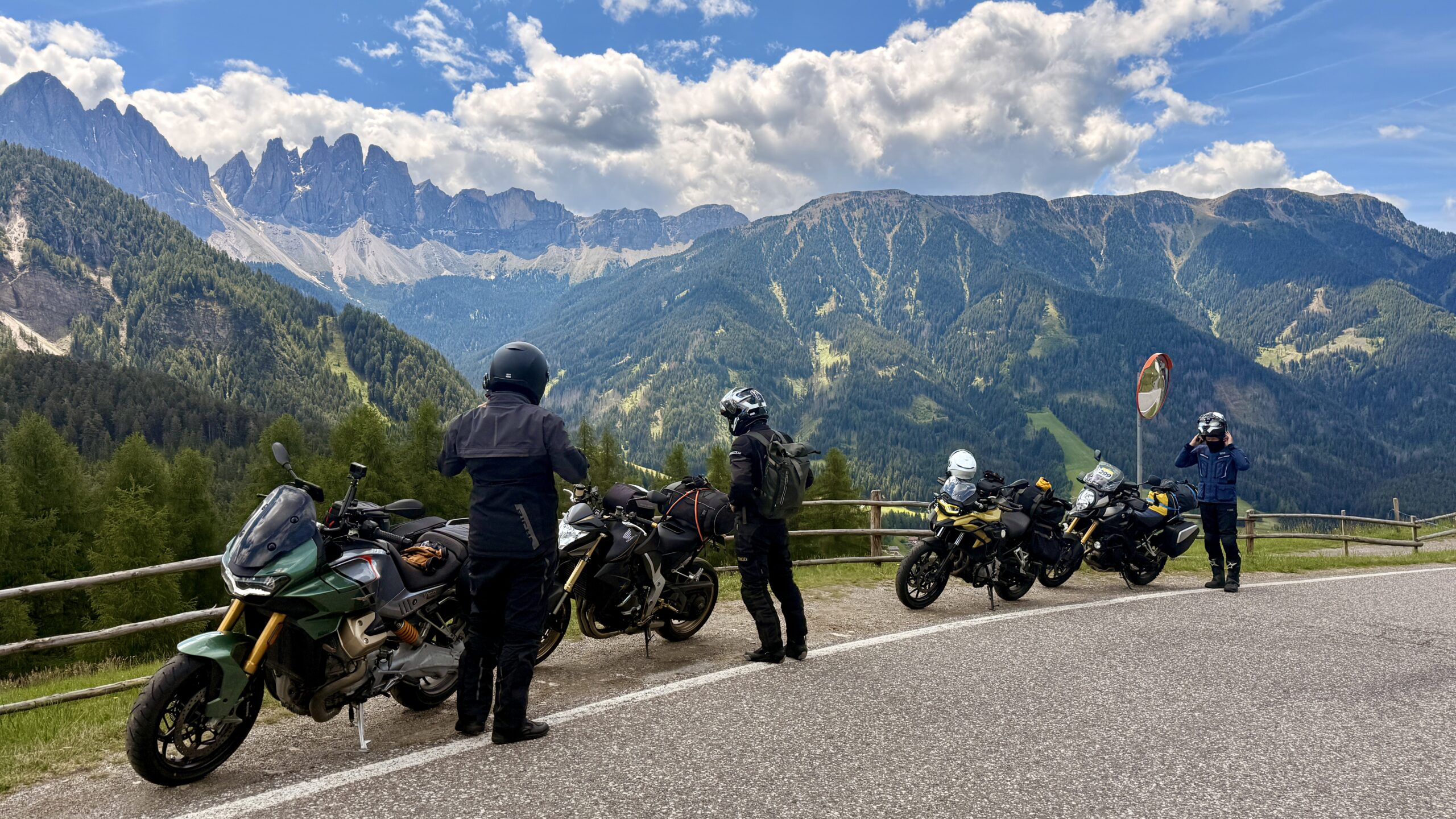 Vier Motorradfahrende machen Pause an einem Aussichtspunkt mit Blick auf die Dolomiten