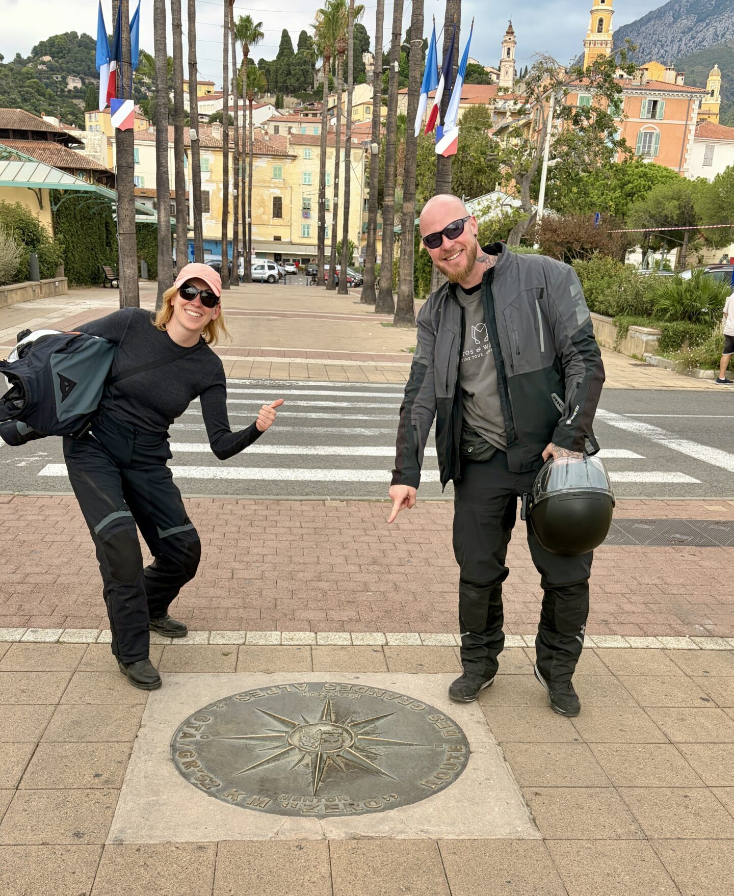 Dominik und Paulina von Motos & Wonders an der Zieltafel der Route des Grandes Alpes in Menton